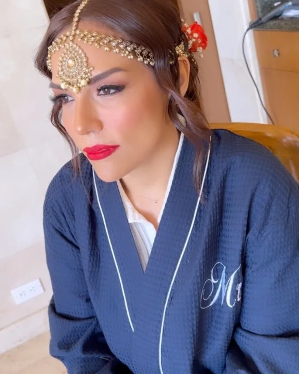 A bride in a jeweled maang tikka with a bold red lip.