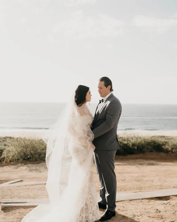 A bride and groom on a windswept bluff above the ocean.