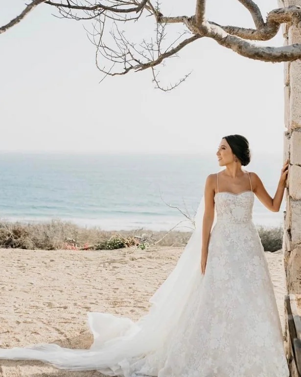 A bride in a strapless gown on the coast, framed by a desert tree.